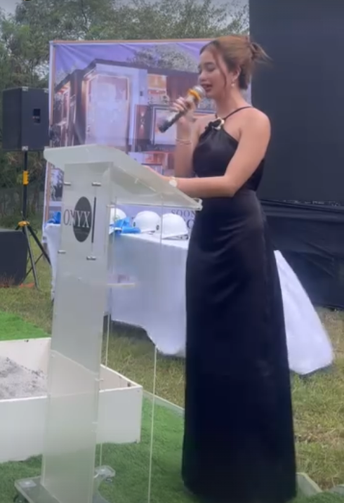 Nicci hosting an outdoor event, speaking into a microphone beside a clear lectern